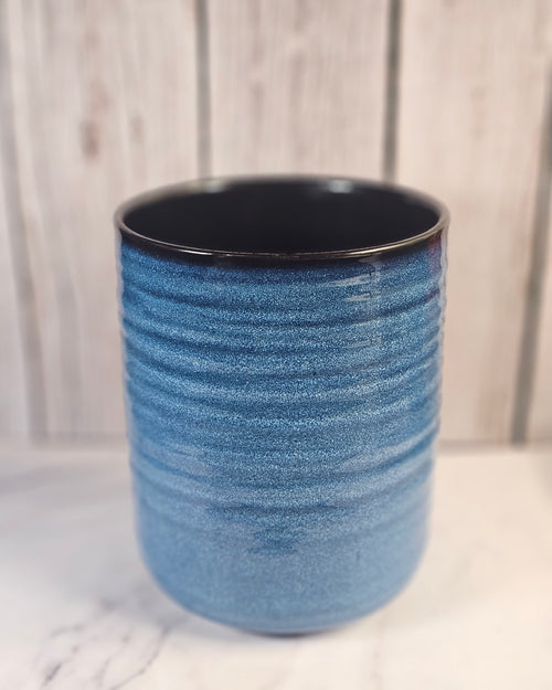 Large empty blue and black candle container sitting in front of a wooden background