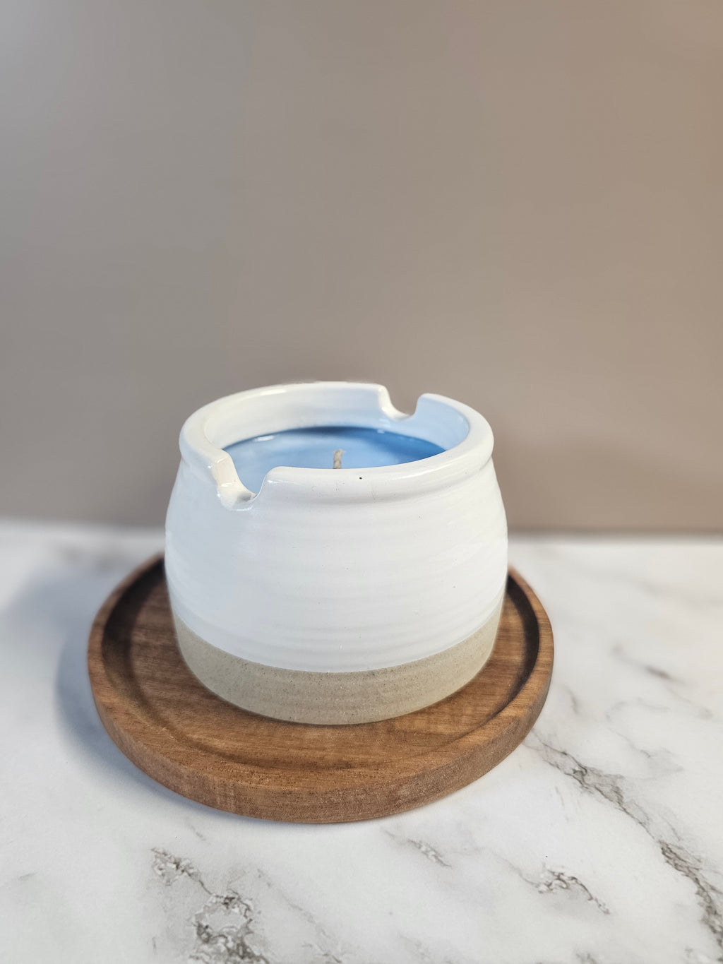 White candle sitting on a wooden base, on a marble surface.