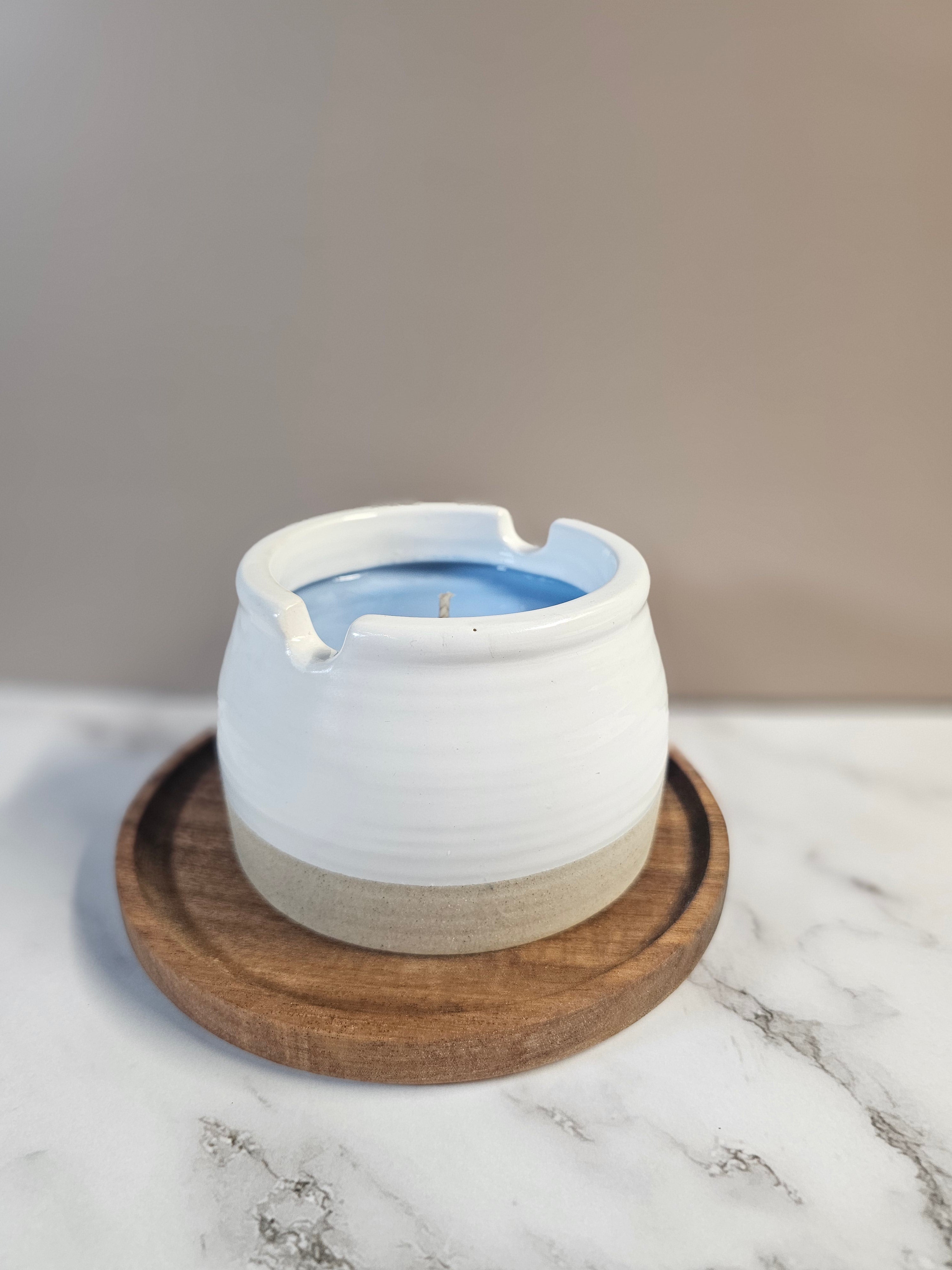 White candle sitting on a wooden base, on a marble surface.