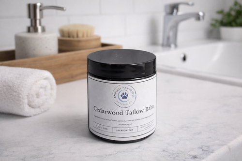 Jar of Cedarwood Tallow Balm on a bathroom counter with a sink and towel in the background.