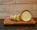 Wooden brush and ramekin of citrus dish soap on a wooden board with a wooden background