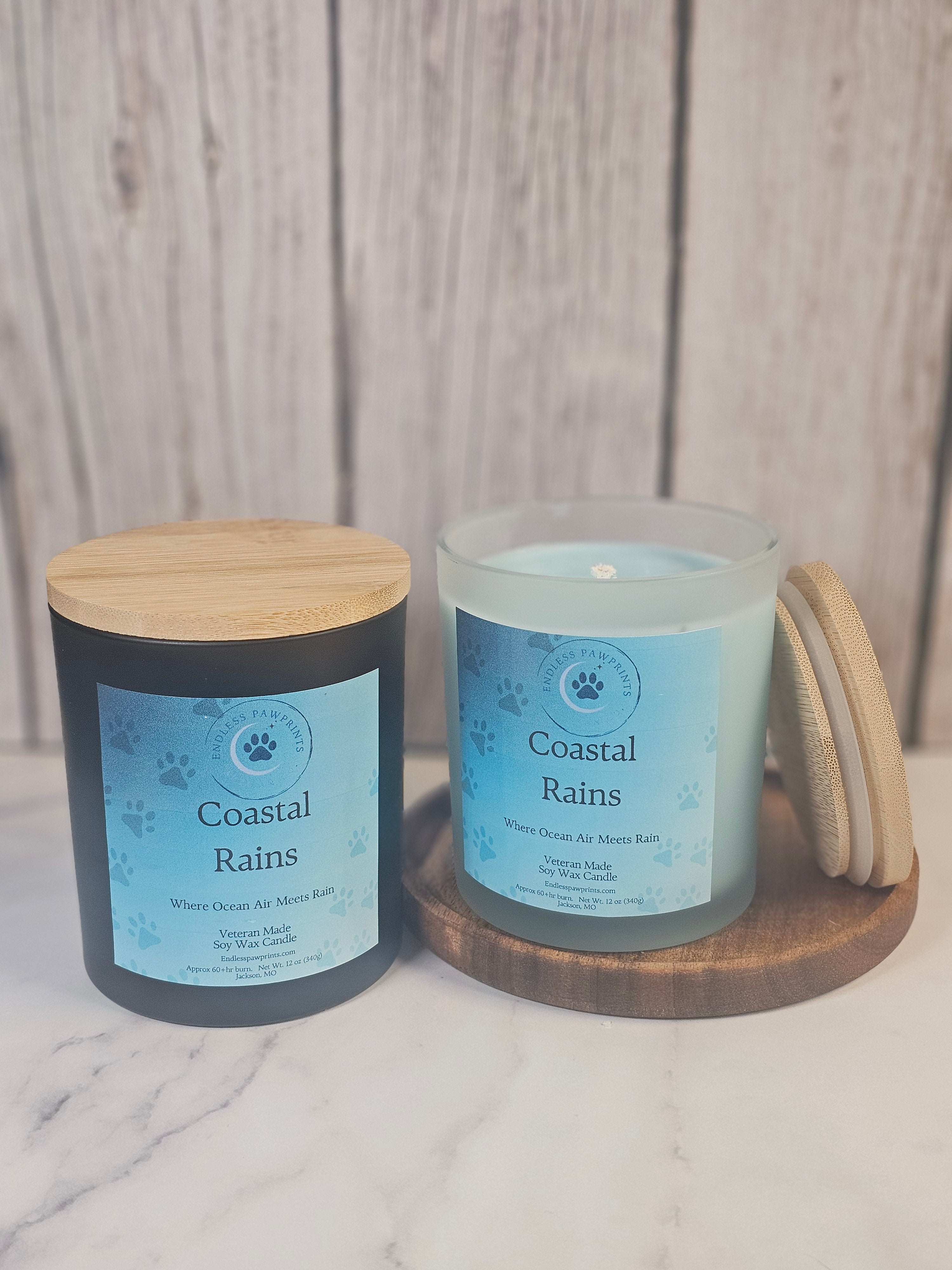 Two candles labeled 'Coastal Rains' with wooden lids on a wooden surface.