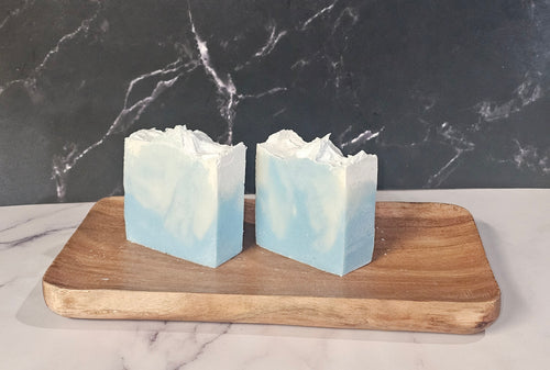 Two bars of coastal rains soap on a wooden board with a marble background