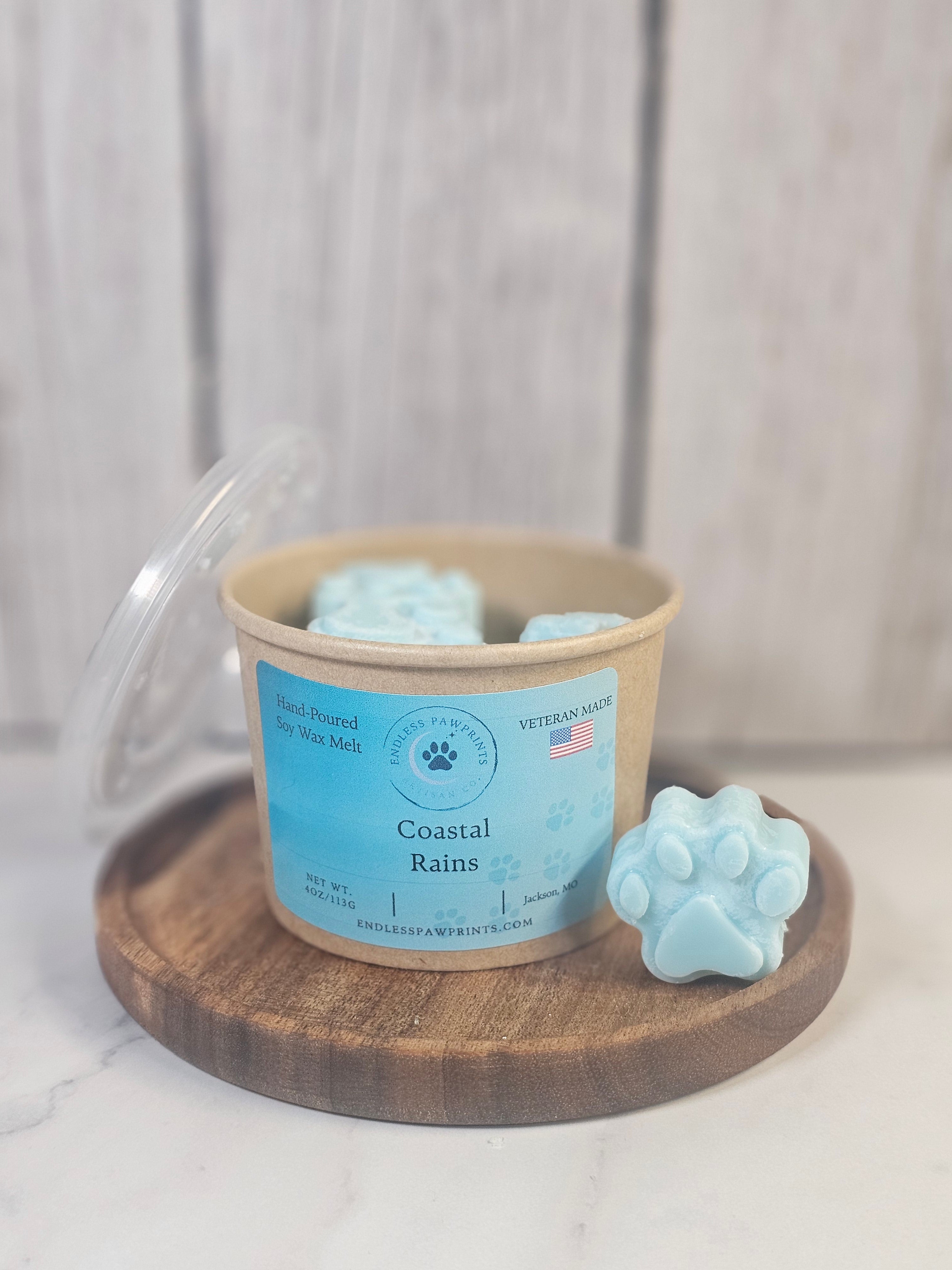Coastal rains paw print wax melts in a craft container sitting on a wooden tray in front of a wooden background.