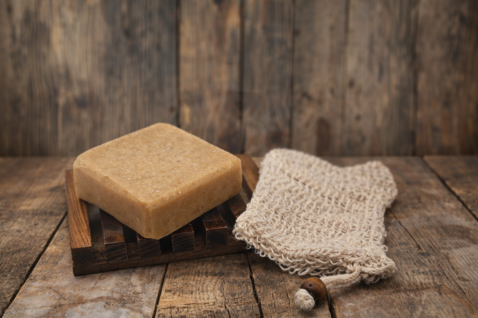 Bar of soap on a wooden soap dish with a natural fiber soap bag on a rustic wooden background