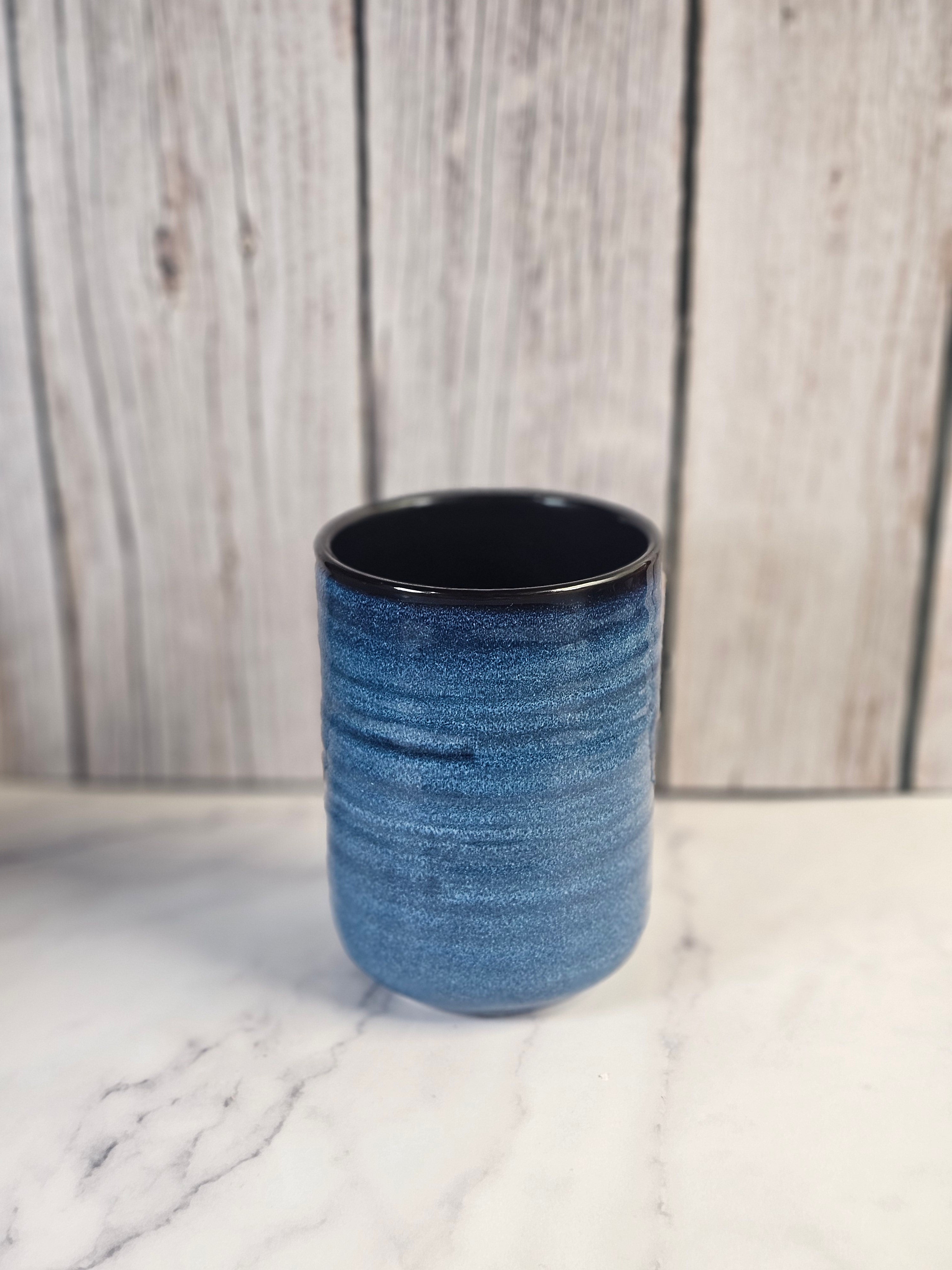 Small 24oz blue and black candle container sitting on a marble counter with a wooden background.