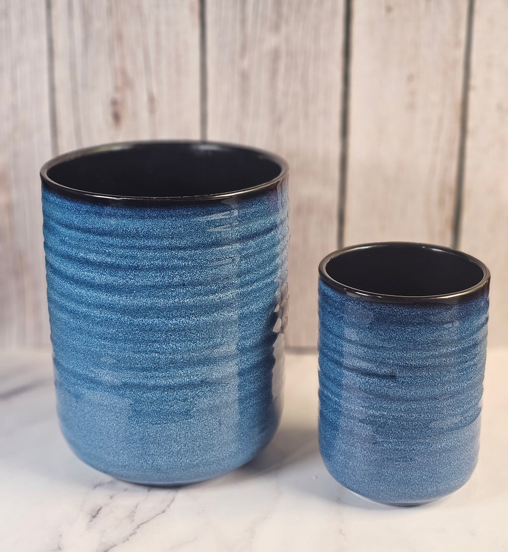 Two blue and black empty candle containers sitting in front of a wooden back ground