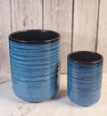 Two blue and black empty candle containers sitting in front of a wooden back ground