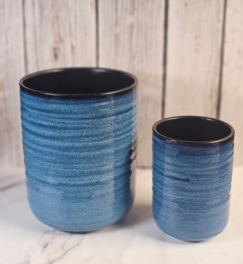 Two blue and black empty candle containers sitting in front of a wooden back ground