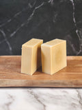 Two bars of unscented soap on a wooden soap dish against a marble and black stone background