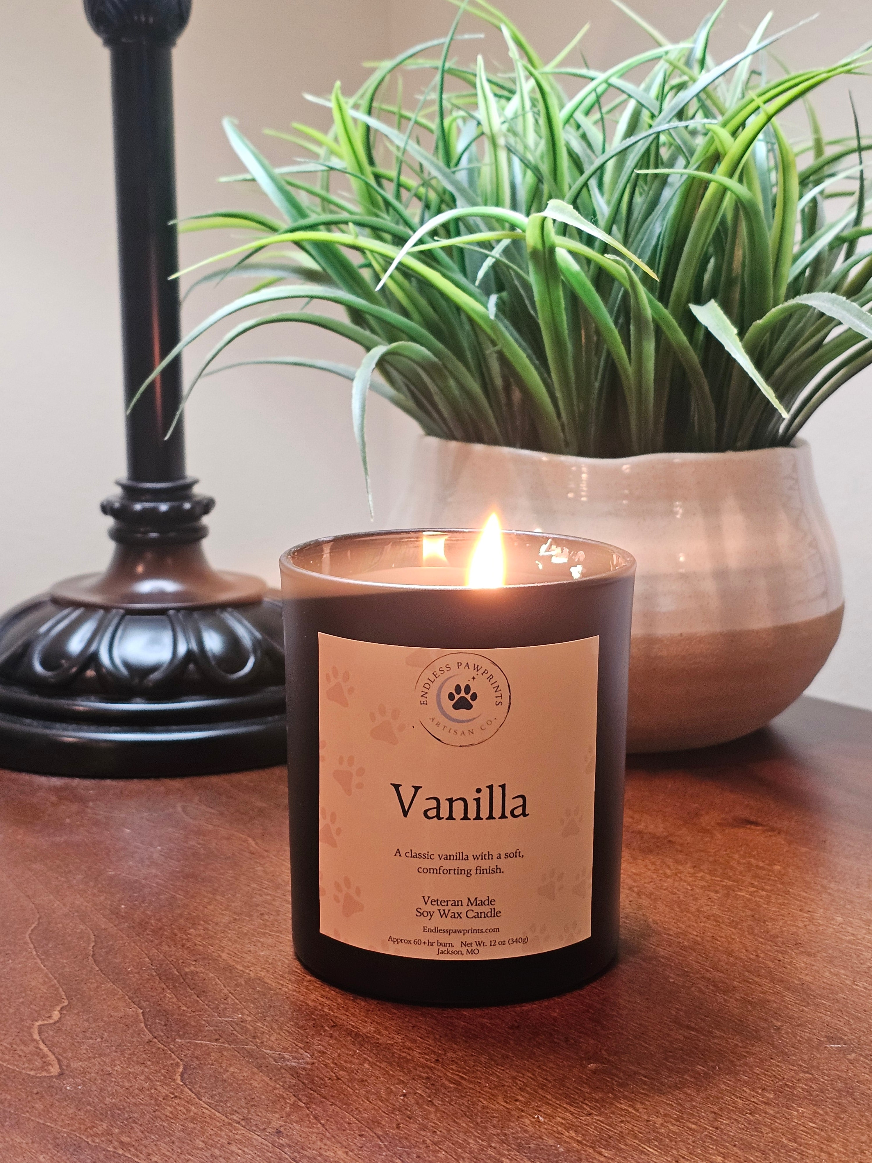 Vanilla scented candle sitting on a wooden end table in front of a plant and lamp