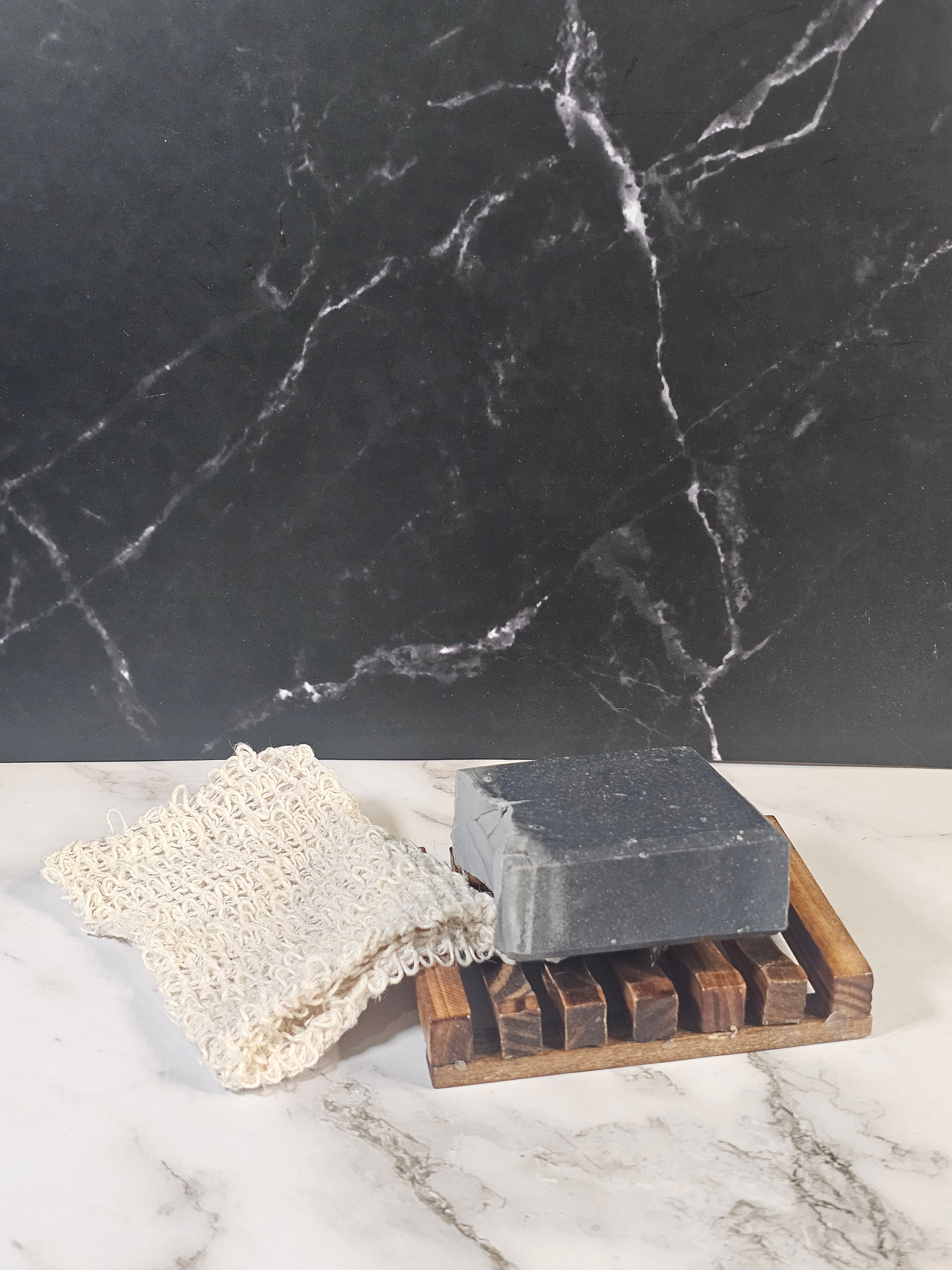 Black marble surface with a wooden soap dish holding a bar of soap and a white loofah.